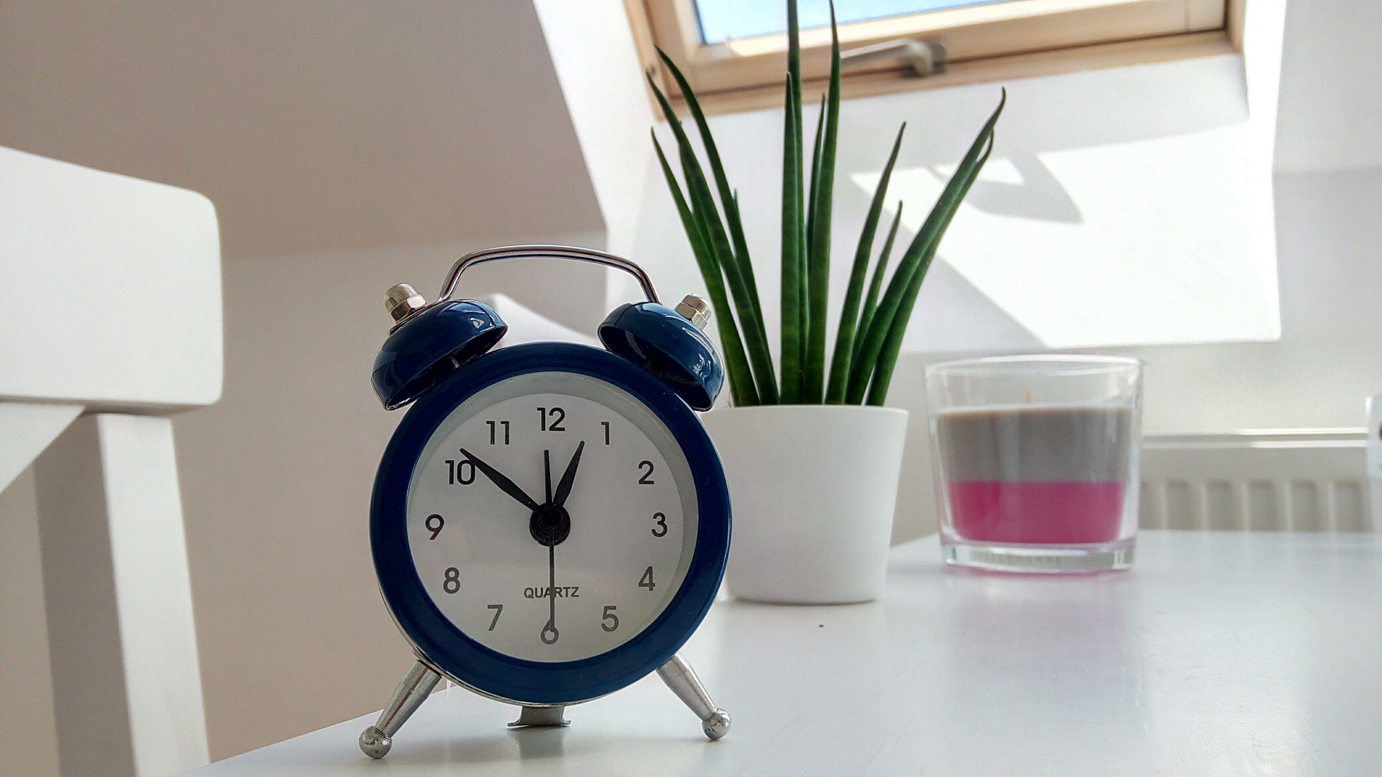dark blue alarm clock on top of white table beside the glass window with white vase green plant timers for bullet journal tools